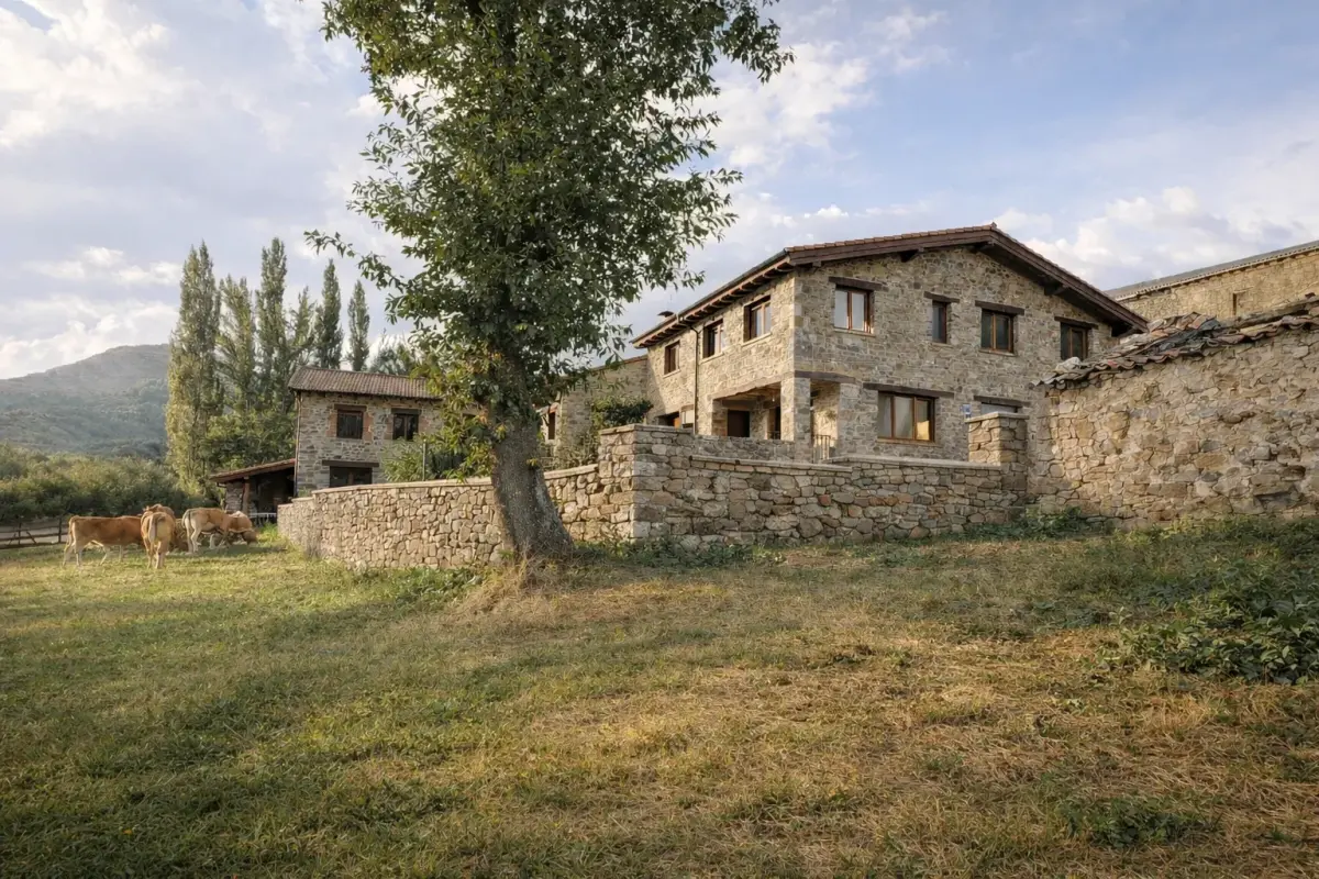 La casa de Cumbres de Lores, de piedra, con vacas pastando en el prado de delante